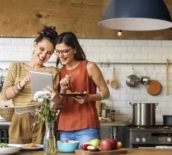 Dos mujeres preparando una comida saludable mientras siguen las recomendaciones de un asesor nutricional profesional en una cocina moderna